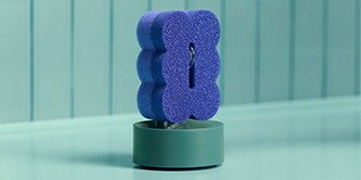 Éponge Brite by Scotch-Brite™ violette pour récurer et essuyer, fixée sur un porte-éponge près de l'évier.
