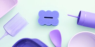 Éponge Brite by Scotch-Brite™ violette pour récurer et essuyer, présentée aux côtés d'ustensiles de cuisine aux couleurs pastel sur le plan de travail.
